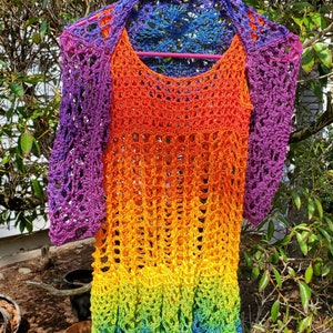 May include: A rainbow crochet top with a crocheted lace trim. The top is made with a gradient of colours, starting with purple and ending with blue. The top is hanging on a pink hanger.
