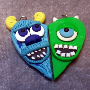 May include: A blue and green heart-shaped charm with the faces of Sully and Mike from Monsters Inc. The charm is made of polymer clay and has a detailed design.