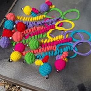 May include: A collection of colorful crocheted cat toys with bells. The toys are made with bright colors like pink, green, yellow, blue, and purple. Each toy has a bell attached to the end.