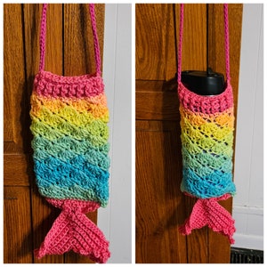 May include: A crocheted mermaid tail-shaped bottle holder with a rainbow color pattern. The holder has a pink strap and a pink tail fin.