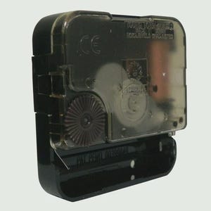 May include: A black plastic quartz clock movement mechanism with a translucent cover. The casing features molded text including Young Town Quartz, Made in Taiwan, No Jewels Unadjusted, and CE. A dark brown gear is visible on the side.