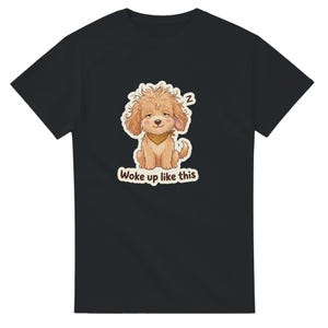 May include: A black short-sleeved t-shirt featuring a graphic of a sleepy, fluffy light brown puppy wearing a tan bandana. The puppy has messy fur, half-closed eyes, and a small 'z' symbol above its head. Below the puppy, the text reads 'Woke up like this'.