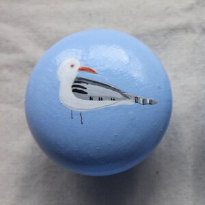 May include: Four light blue round wooden knobs with painted seagull designs. Each knob features a white seagull with black markings and an orange beak.