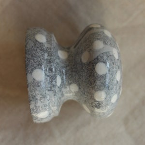 May include: A gray ceramic knob with white polka dots. The knob is round and has a small stem.