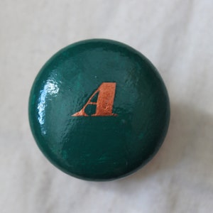 May include: A round, green bottle stopper with a copper-coloured letter 'A' on top.