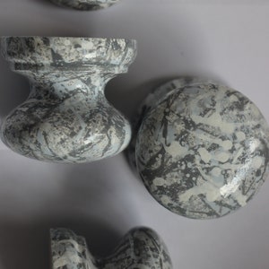 Może przedstawiać: Cztery ceramiczne gałki do szafek w kolorze szarym i białym z wzorami w kropki. Gałki są okrągłe i mają podniesiony brzeg.