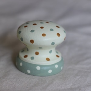 Puede incluir: Pomo de armario decorativo con forma de hongo. El pomo está pintado de color blanquecino con lunares marrones y verde azulado en la parte superior. La base es verde azulado con lunares blancos. Este pomo único es perfecto para añadir un toque de fantasía a los muebles.