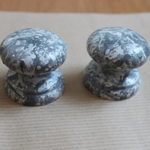May include: Two gray ceramic cabinet knobs with a white splatter paint design.