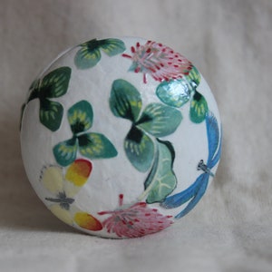 May include: A white sphere with a painted design of green shamrocks, blue dragonflies, and pink flowers.