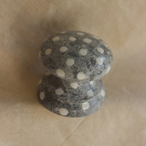 Könnte beinhalten: Ein grauer Keramik-Knopf mit weißen Punkten. Der Knopf ist rund und hat einen kurzen Stiel.