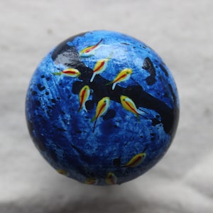 May include: A blue and black sphere with a painted design of yellow and red fish. The sphere is painted to look like an underwater scene.