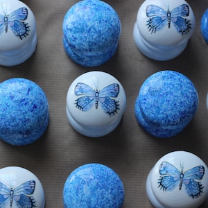 Puede incluir: Una colección de 12 pomos redondos de cerámica blanca con diseños de mariposas azules. Cada pomo tiene un acabado moteado azul y blanco.