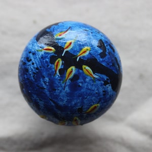 May include: A blue and black sphere with a painted design of yellow and red fish. The sphere is painted to look like an underwater scene.