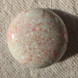 May include: A round, smooth, speckled stone with a light green base and red and white speckles.