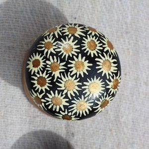 Könnte beinhalten: Zwei bemalte runde Steine. Ein Stein ist schwarz mit weißen und goldenen Gänseblümchen. Der andere Stein ist dunkelgrün mit goldenen Punkten.