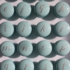Puede incluir: Veintiséis pomos redondos de color azul claro con letras plateadas que deletrean el alfabeto de la a a la z.