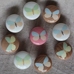 Puede incluir: Nueve pomos de madera con diseños de mariposas. Los pomos están pintados en varios colores, incluyendo rosa, azul, verde y amarillo. Las mariposas tienen diferentes patrones de alas y colores.