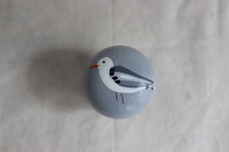 K&ouml;nnte beinhalten: Ein handbemalter grauer Stein mit einer darauf gemalten wei&szlig;en M&ouml;we. Die M&ouml;we hat schwarze Augen und einen roten Schnabel.