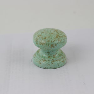 May include: A small, round, green cabinet knob with a speckled, gold-coloured paint finish.