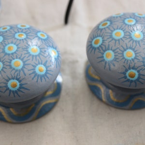 Peut inclure: Deux boutons en bois peints en gris avec des motifs en étoile bleu et or. Les boutons ont une base ondulée bleu et or.