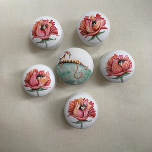 Puede incluir: Seis piedras decorativas redondas blancas. Cinco piedras presentan un dise&ntilde;o floral rojo y rosa. La sexta piedra tiene una criatura parecida a un caballito de mar sobre un fondo turquesa. Las piedras est&aacute;n pintadas a mano.