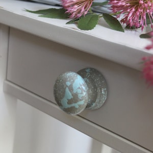 May include: A white painted wooden drawer with two round knobs. The knobs are painted a light gray with blue splatter paint.