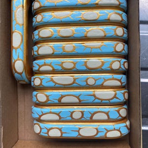 Può includere: Una tazza decorativa con un motivo a raggi di sole blu, bianco e oro. La tazza è in legno e ha un manico. La tazza è in una scatola di cartone.