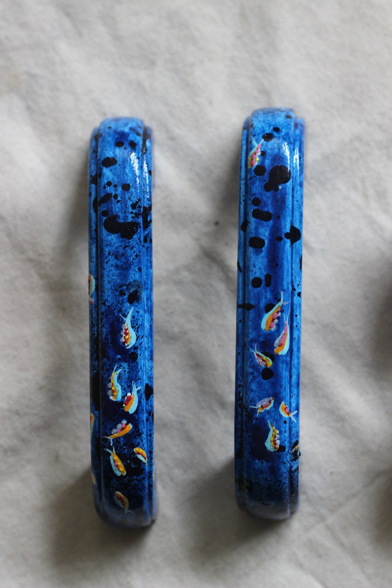 May include: Two blue painted cabinet door pulls with a design of small yellow and orange fish on a blue background.
