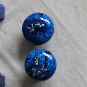 May include: Two blue round knobs with a speckled finish and painted yellow and orange fish designs.