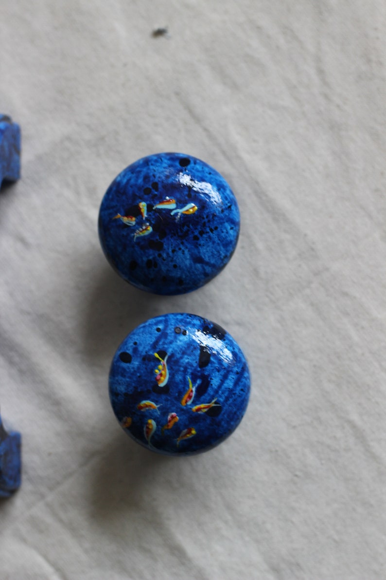 May include: Two blue round knobs with a speckled finish and painted yellow and orange fish designs.