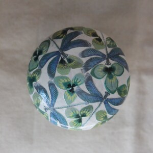 Può includere: Un ornamento rotondo in ceramica bianca con un design di libellula e fiori blu e verdi.
