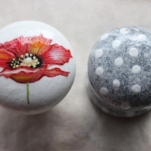 Könnte beinhalten: Zwei runde Keramikknöpfe, einer mit weißem Hintergrund und einer darauf gemalten roten Mohnblume, der andere mit grauem Hintergrund und weißen Punkten.