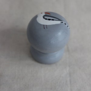 K&ouml;nnte beinhalten: Ein grauer Keramik-Knopf mit einem bemalten wei&szlig;en M&ouml;wen-Design. Die M&ouml;we hat schwarze Augen und einen roten Schnabel.