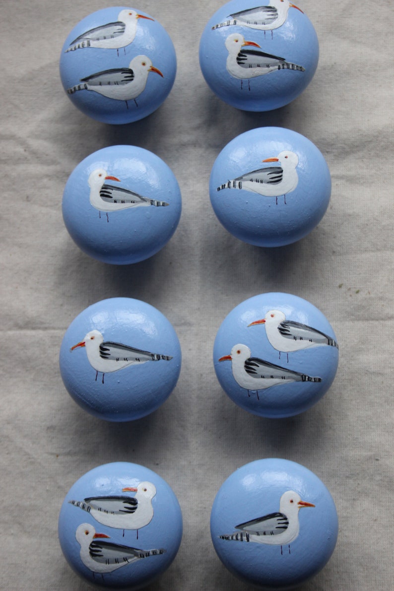 May include: Eight blue round knobs with painted seagull designs. Each knob features a white seagull with black markings and orange beak on a light blue background.