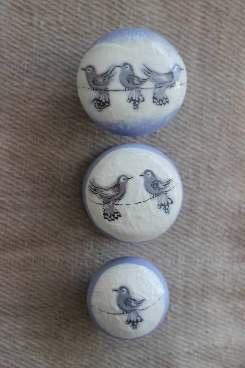 May include: Three circular decorative items with a white surface and a pale blue border. Each features a hand-painted design of grey birds on a wire. The birds have detailed wings and are arranged in different groupings.