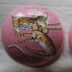 Peut inclure: Une d&eacute;coration ronde en c&eacute;ramique rose avec une image peinte de deux l&eacute;opards. Les l&eacute;opards sont brun et noir avec des taches blanches. Un l&eacute;opard est enroul&eacute; et l'autre est couch&eacute; sur le dessus.