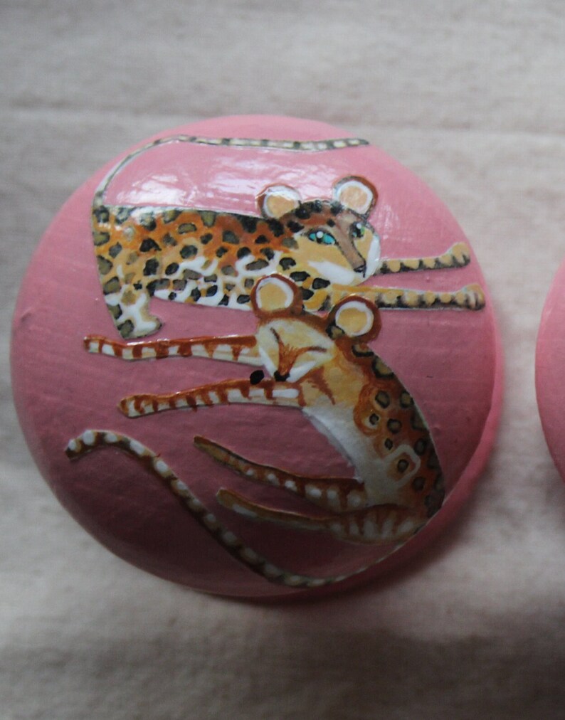 Peut inclure: Une d&eacute;coration ronde en c&eacute;ramique rose avec une image peinte de deux l&eacute;opards. Les l&eacute;opards sont brun et noir avec des taches blanches. Un l&eacute;opard est enroul&eacute; et l'autre est couch&eacute; sur le dessus.