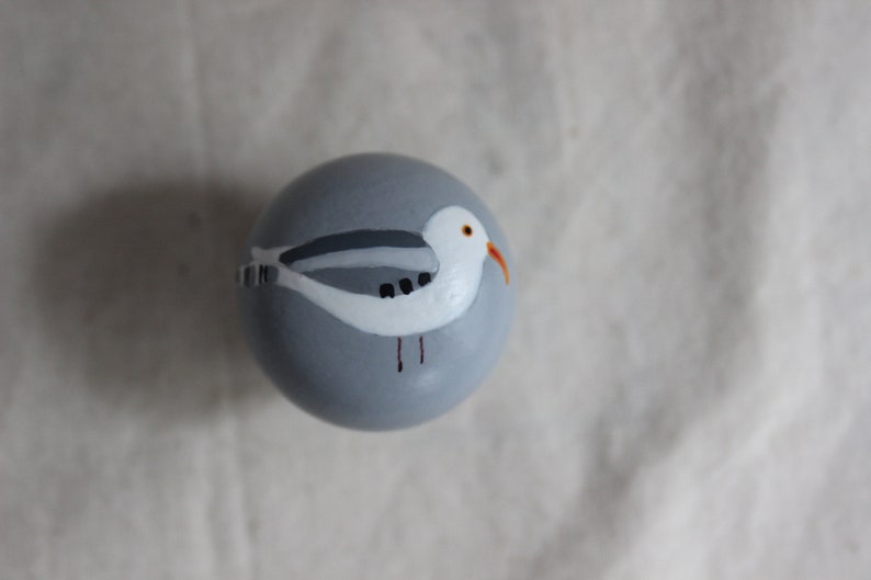 K&ouml;nnte beinhalten: Eine graue bemalte Kugel mit einer darauf gemalten wei&szlig;en M&ouml;we. Die M&ouml;we hat einen grauen R&uuml;cken, einen wei&szlig;en Bauch und einen orangefarbenen Schnabel.