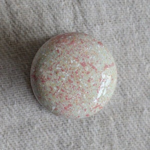 Könnte beinhalten: Ein runder, gesprenkelter Stein mit einer hellgrünen Basis und roten und weißen Flecken.