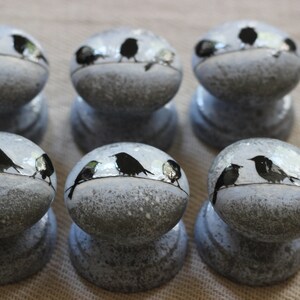 K&ouml;nnte beinhalten: Sechs graue Keramikkn&ouml;pfe mit wei&szlig;er Waschung. Jeder Knopf zeigt eine schwarze Silhouette von drei V&ouml;geln, die auf einem Draht sitzen.