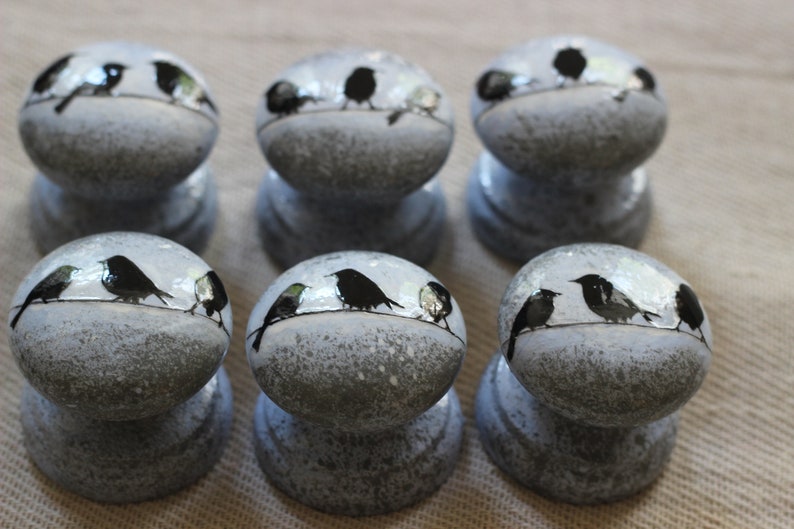 K&ouml;nnte beinhalten: Sechs graue Keramikkn&ouml;pfe mit wei&szlig;er Waschung. Jeder Knopf zeigt eine schwarze Silhouette von drei V&ouml;geln, die auf einem Draht sitzen.