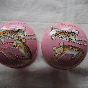 Peut inclure: Deux ornements ronds roses avec des images peintes de l&eacute;opards. Les l&eacute;opards sont dans diff&eacute;rentes poses, certains sont enroul&eacute;s et d'autres sont allong&eacute;s.