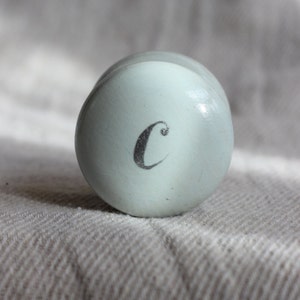 Puede incluir: Un recipiente redondo de color azul claro con una letra "C" blanca en la parte superior.