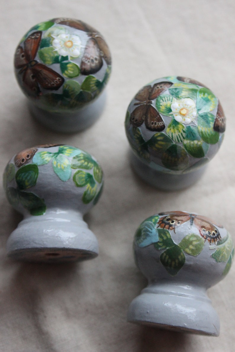 Puede incluir: Cuatro pomos de cer&aacute;mica con una base gris claro y un dise&ntilde;o de mariposa y flor blanco, verde y marr&oacute;n.