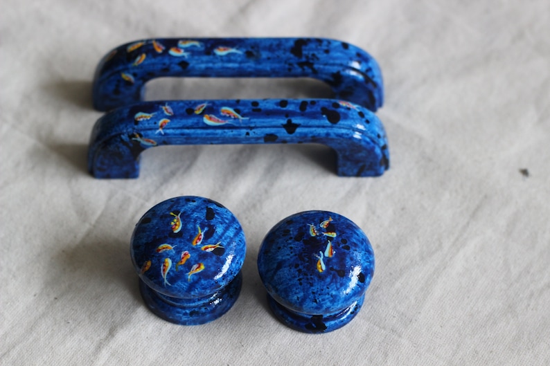 May include: Set of four blue cabinet knobs and pulls with a splatter paint design and small orange fish painted on them.