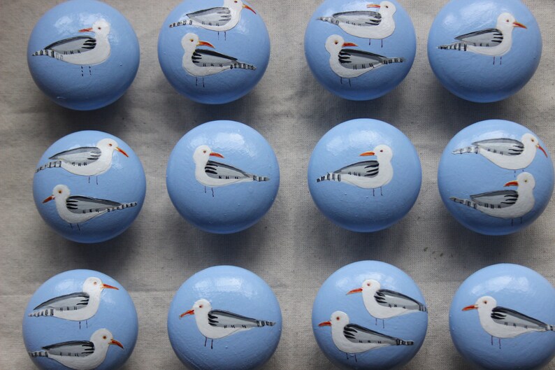 May include: Twelve blue ceramic knobs with white painted seagulls. Each knob features a different seagull design.