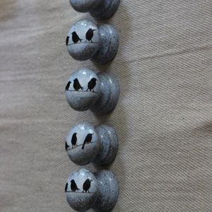 K&ouml;nnte beinhalten: Sechs blaue und graue bemalte Holzkn&ouml;pfe mit schwarzen Silhouetten von V&ouml;geln, die auf einem Ast sitzen.