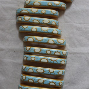 May include: A stack of 12 blue and gold painted drawer pulls with a white sunburst design. The pulls are arranged in a vertical stack, with the top pull at the top of the image and the bottom pull at the bottom of the image.