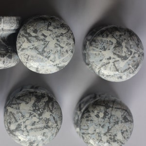 Könnte beinhalten: Vier runde, graue und weiße Keramikknöpfe mit einem gesprenkelten Muster. Die Knöpfe sind in einer quadratischen Form angeordnet.