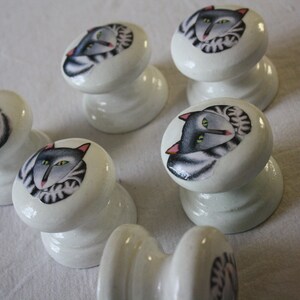Puede incluir: Seis pomos de cajón de cerámica blanca con un diseño de gato gris y blanco. Cada pomo tiene un diseño de gato diferente.